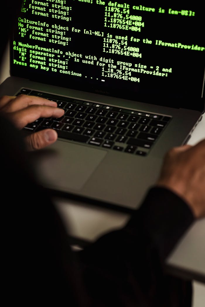 services-01 Crop anonymous male cyber spy hacking portable computer with codes on screen while sitting at table